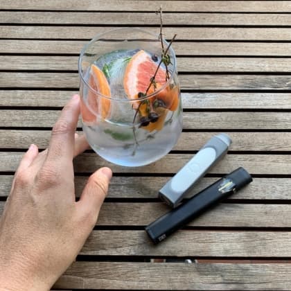 Gray POCKET personal filter next to a vape on a table beside a grapefruit drink